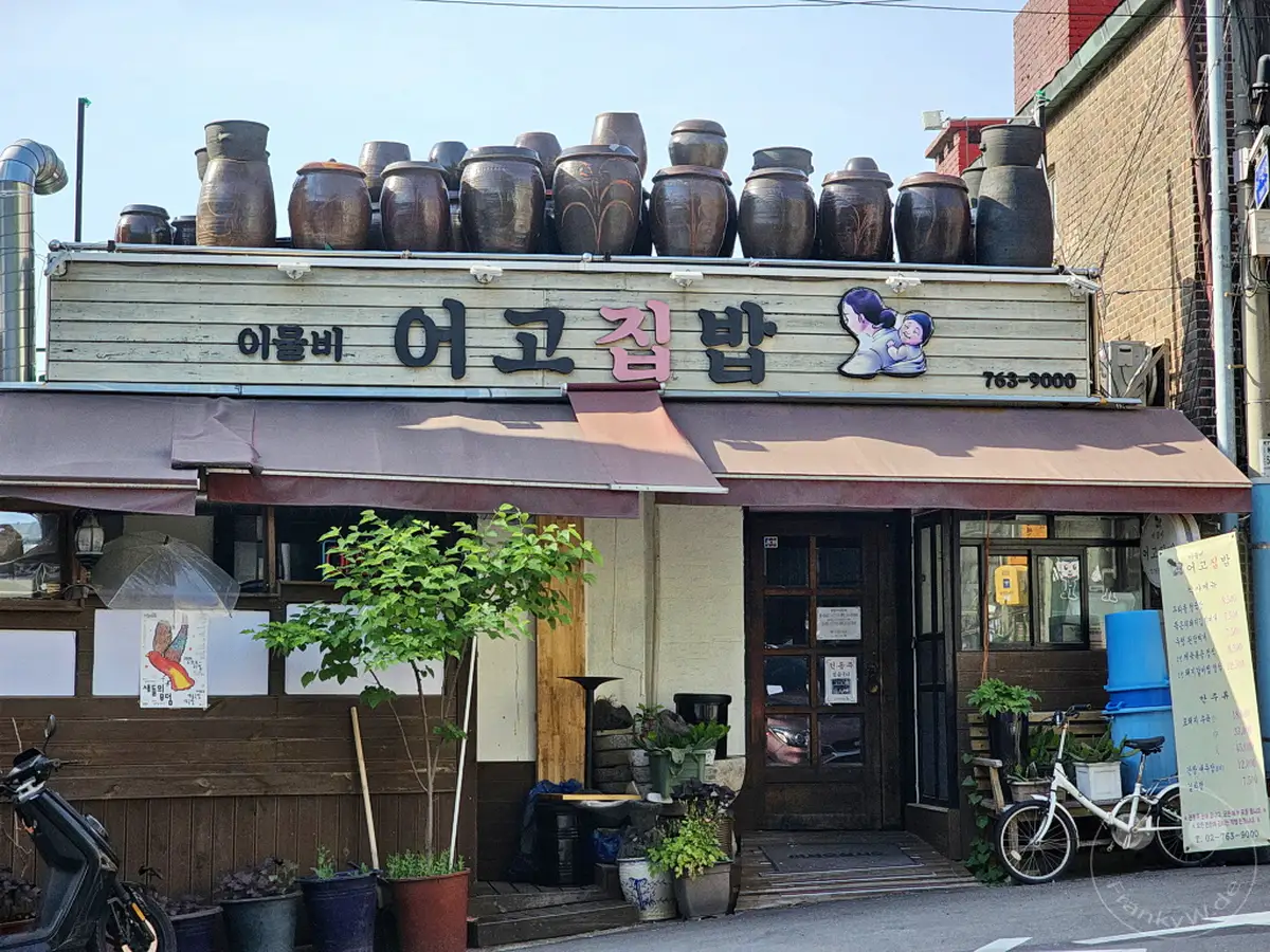 Ein traditionelles koreanisches Restaurant im Daehangno district in Seoul, Südkorea, präsentiert eine Fassade geschmückt mit zahlreichen Keramiktöpfen auf dem Dach. Die einladende Aufmachung suggeriert authentische koreanische Gastfreundschaft und kulinarische Erlebnisse. Die sonnige Atmosphäre spiegelt die Lebendigkeit des Viertels wider.