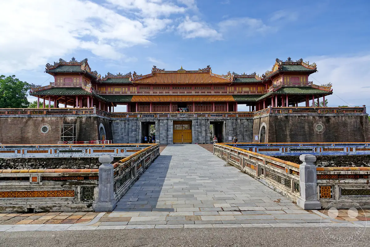 Die Ngo Mon (Südtor) der Kaiserstadt Hue in Vietnam ist ein imposantes Bauwerk und diente als Haupteingang zur Verbotenen Stadt. Die traditionelle vietnamesische Architektur mit ihren geschwungenen Dächern und ornamentalen Verzierungen spiegelt die historische Bedeutung des Ortes wider. Die weite, gepflasterte Brücke führt direkt auf das monumentale Tor zu und vermittelt eine feierliche Atmosphäre unter dem blauen Himmel mit vereinzelten Wolken.