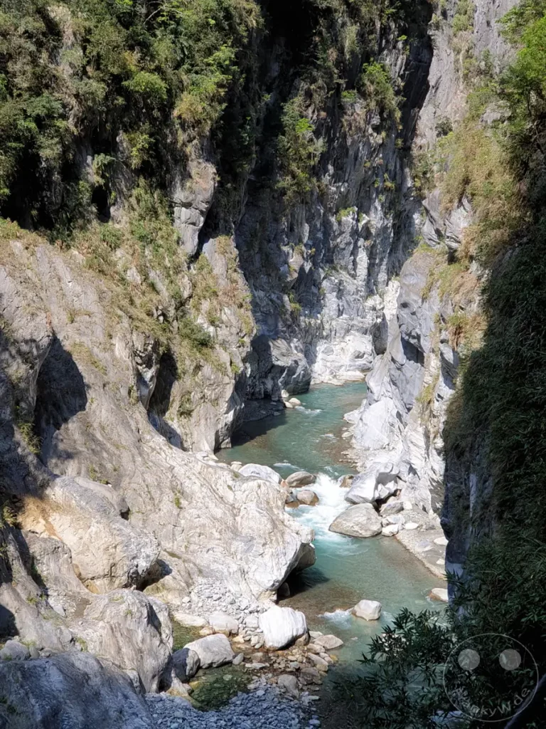 Der Taroko-Nationalpark in Taiwan präsentiert den atemberaubenden Tunnel of Nine Turns, eine enge Schlucht, durch die sich ein türkisfarbener Fluss schlängelt. Mächtige Felswände, von Vegetation bedeckt, steigen steil empor und formen eine dramatische Landschaft. Das klare Wasser und die majestätische Umgebung erzeugen ein Gefühl von unberührter Natur und Erhabenheit.