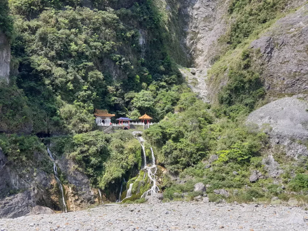 Der Changchun Schrein (ewige Frühlings-Schrein) ist in den Taroko Nationalpark in Taiwan eingebettet, umgeben von steilen Berghängen. Wasserfälle stürzen von den begrünten Felswänden herab und sammeln sich in einem Flussbett aus Flusskieseln. Die traditionelle Architektur des Schreins hebt sich harmonisch von der dramatischen Naturszenerie ab.