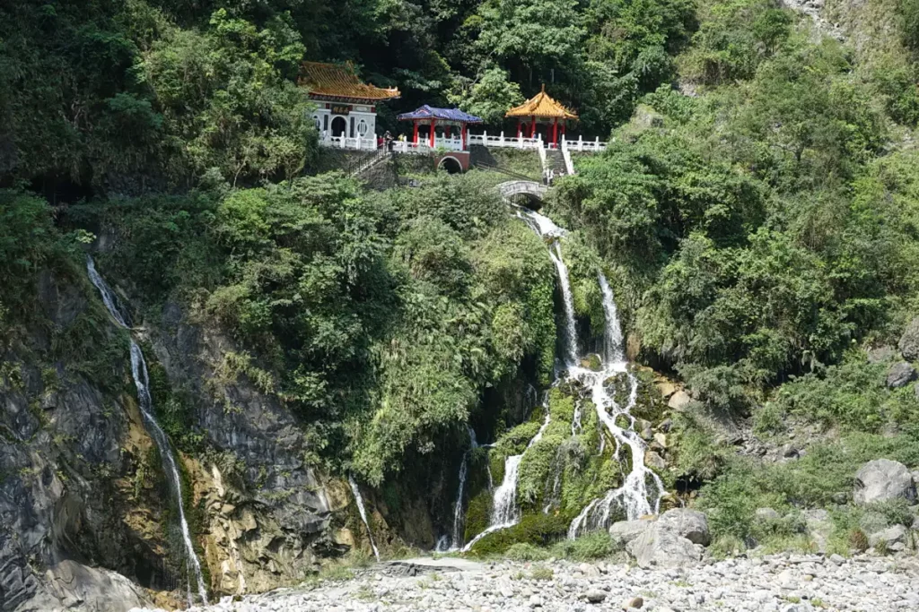 Der Changchun Schrein im Taroko National Park in Taiwan ist ein atemberaubendes Beispiel traditioneller Architektur, eingebettet in eine üppige Berglandschaft. Mehrere Wasserfälle stürzen von den Felswänden herab und münden in einem Bachbett, das von Geröll gesäumt ist. Die friedliche Atmosphäre des Ortes wird durch das Rauschen des Wassers und die natürliche Schönheit der Umgebung unterstrichen.