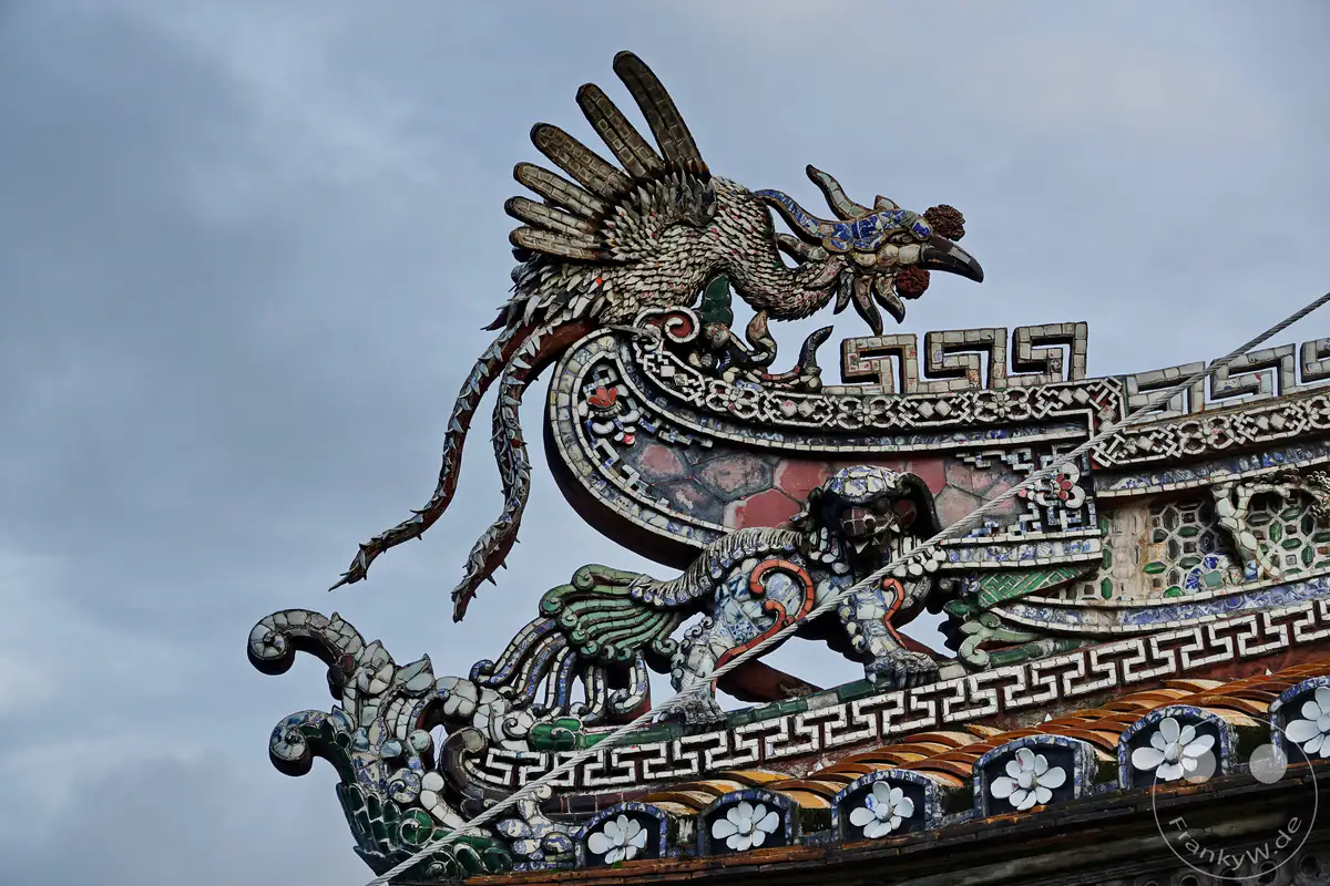 Ein kunstvoll verzierter Dachschmuck aus zerbrochener Keramik ziert die Dächer der Zitadelle in Hue, Vietnam. Drachenfiguren und Fabelwesen im Stil der Kaiserstadt bewachen die historischen Gebäude. Die detaillierte Handwerkskunst und die leuchtenden Farben spiegeln die reiche kulturelle Vergangenheit wider.