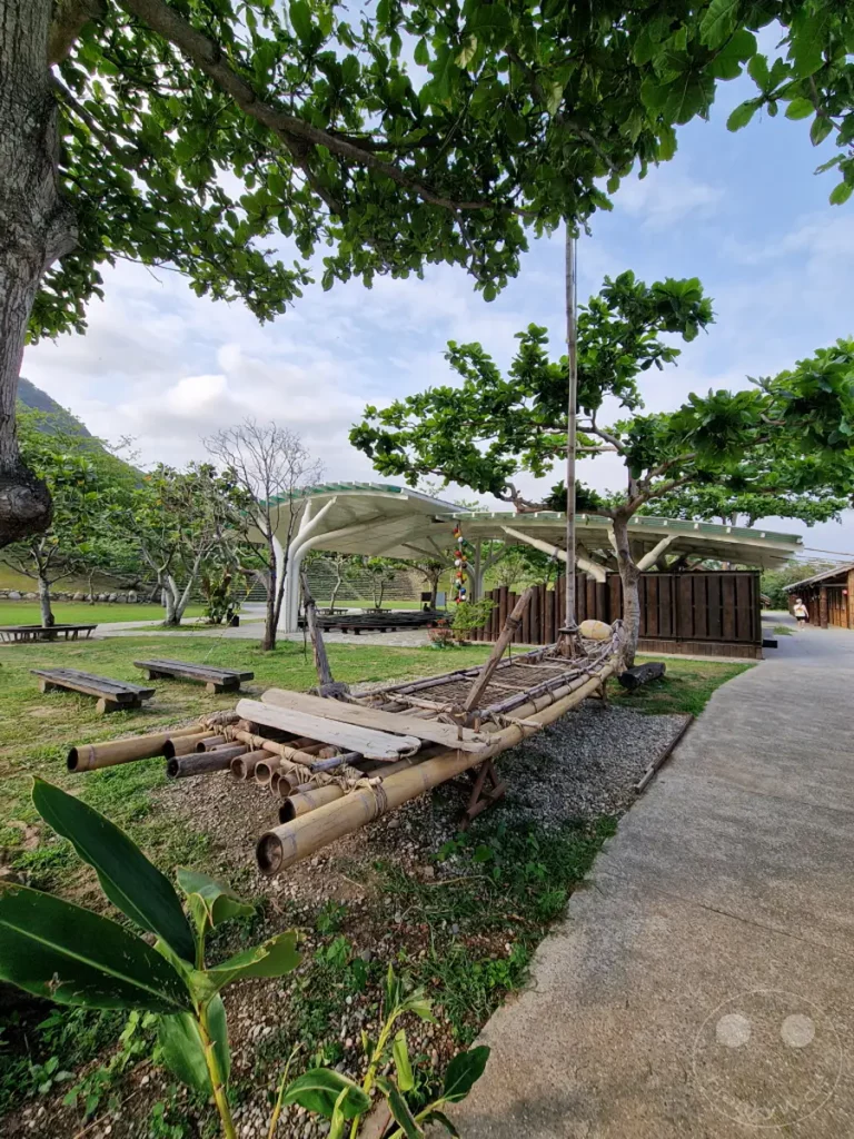 Ein aus Bambus gefertigtes traditionelles Floß liegt auf einer grünen Wiese im Amis Folk Center in Taiwan. Umgeben von üppigem Grün und Bäumen strahlt die Szene eine friedliche und ländliche Atmosphäre aus. Der sonnige Tag und die natürliche Umgebung laden zum Entspannen ein.