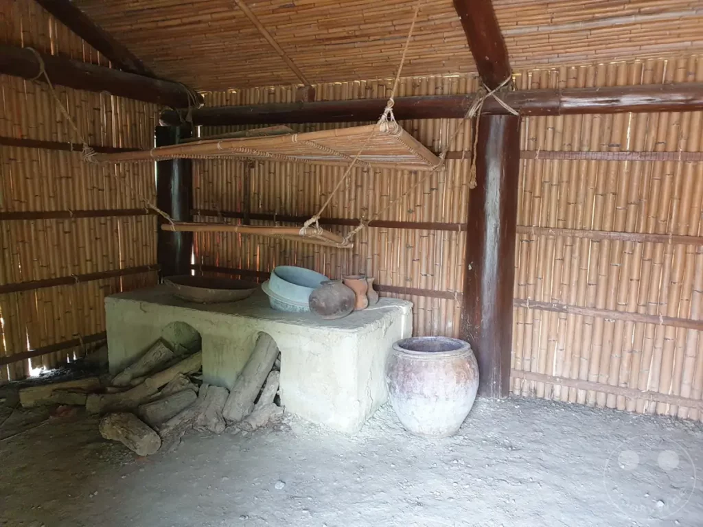 Ein Einblick in ein traditionelles Amis-Haus auf Taiwan im Amis Folk Center, das eine einfache Kochstelle mit Holzscheiten, Töpferwaren und Vorräten zeigt. Die rustikale Konstruktion aus Bambus und Holz vermittelt ein Gefühl von Authentizität und Vergangenheit. Die Szene lädt dazu ein, sich das tägliche Leben der indigenen Bevölkerung vorzustellen.