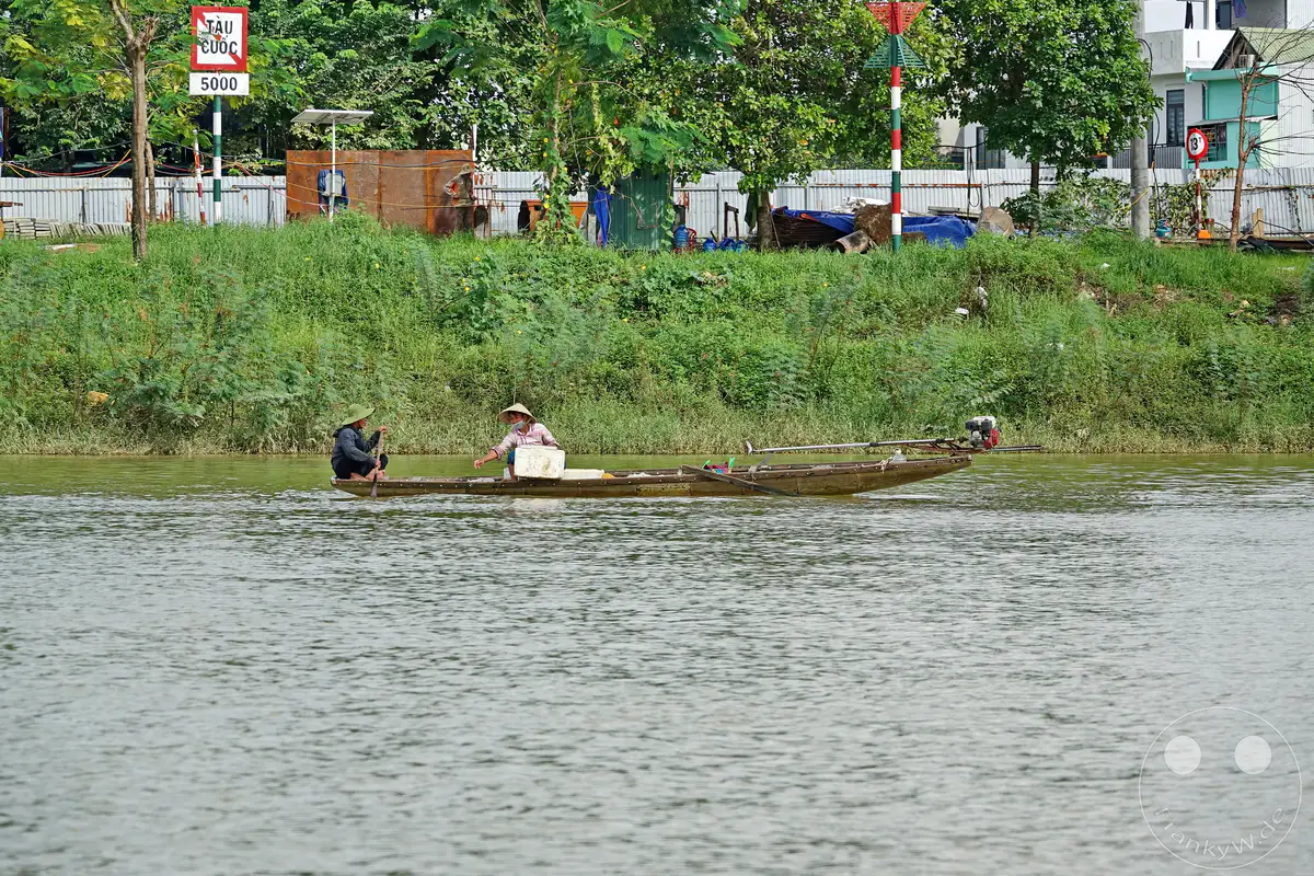 Eine traditionelle Fischerbootfahrt auf dem Fluss der Parfums (Perfume River) in Hue, Vietnam. Zwei Fischer in traditioneller Kleidung sind auf dem Boot unterwegs, eines mit einem Außenbordmotor versehen, um die Arbeit zu erleichtern. Die Szene vermittelt einen Eindruck von Ruhe und dem täglichen Leben am Fluss.