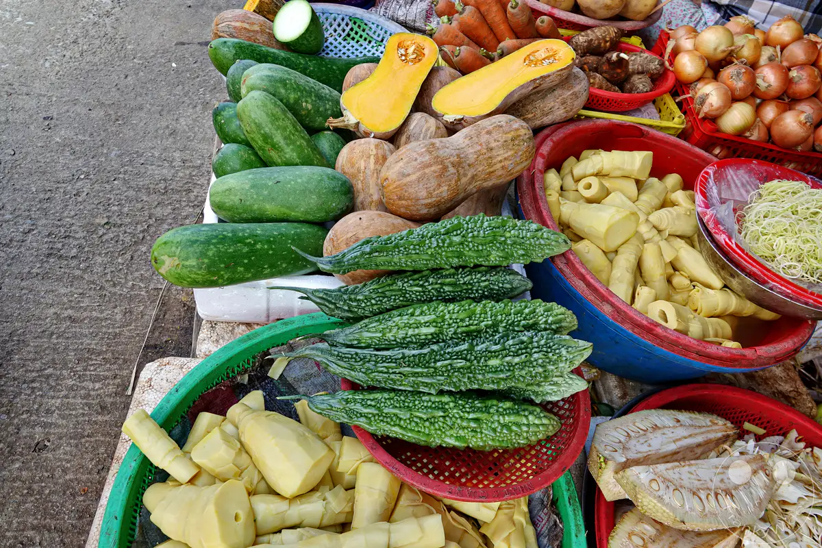 Frisches Gemüse und Obst werden auf einem Straßenmarkt in Hue, Vietnam, zum Verkauf angeboten. Die Vielfalt an Produkten unterstreicht die landwirtschaftliche Fülle der Region. Eine geschäftige und bunte Marktszene, die den Alltag in der Stadt widerspiegelt.