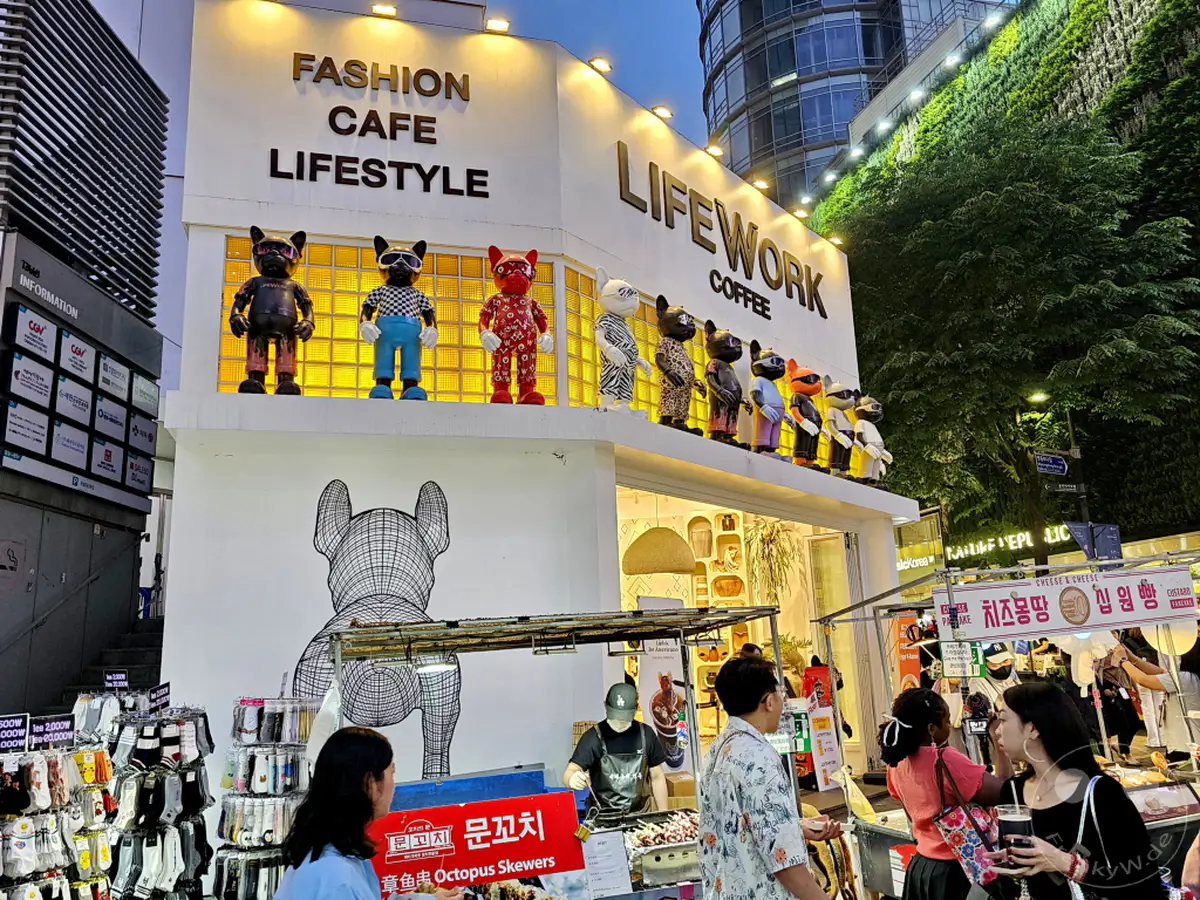 Die belebte Myeongdong Street in Seoul, Südkorea, erstrahlt bei Nacht in voller Pracht. Einladende Geschäfte mit stilvollen Dekorationen, darunter Figuren im Comic-Stil, säumen die Straße. Verschiedene Stände locken mit kulinarischen Genüssen und bieten ein lebendiges Einkaufserlebnis.