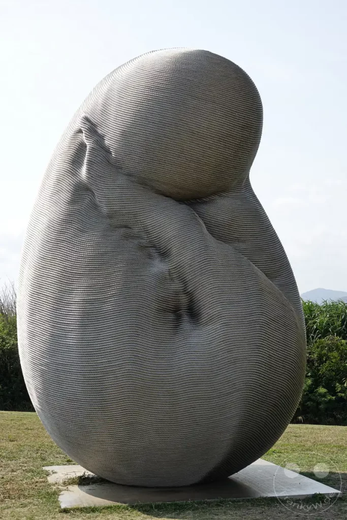 Eine auffällige Skulptur aus miteinander verdrillten Drähten steht auf einer Grasfläche in der Nähe des Eluanbi Leuchtturms in Taiwan. Die organische, eggenförmige Form scheint sich aus sich selbst heraus zu winden und zu verdichten und erzeugt eine fesselnde visuelle Textur. Die Außenskulptur von Kang Muxiang strahlt eine Aura der Erneuerung und künstlerischen Transformation aus, die in die natürliche Umgebung integriert ist.