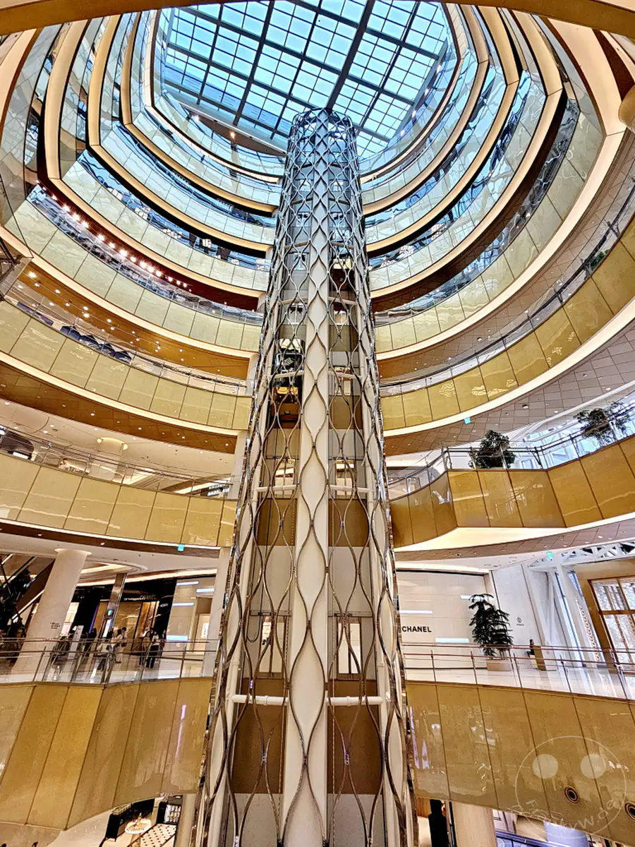 Ein Blick in das Innere des modernen Einkaufszentrums Lotte World Mall in Seoul, Südkorea. Die geschwungenen Ebenen und das zentrale Aufzugssystem schaffen ein beeindruckendes architektonisches Ambiente. Das Glasdach lässt viel natürliches Licht herein und unterstreicht die luxuriöse Atmosphäre des Gebäudes.