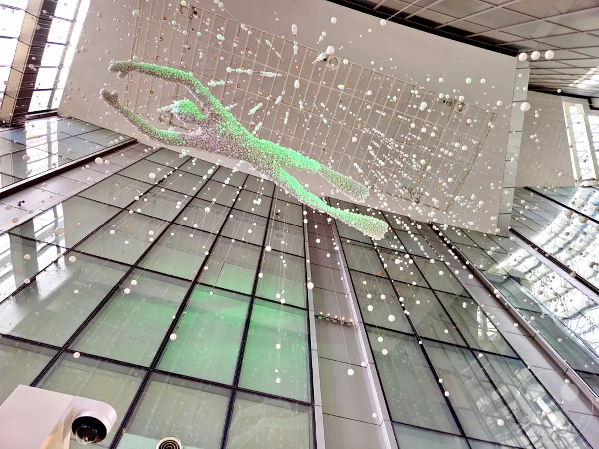 Eine beeindruckende Kunstinstallation eines Schwimmers aus tausenden von kleinen Kugeln hängt von der Decke im Lotte World Tower in Seoul, Südkorea. Hunderte von Kugeln in verschiedenen Größen, aufgehängt an dünnen Fäden, hüllen die Skulptur ein und erzeugen eine schwebende Atmosphäre. Die moderne Architektur mit viel Glas reflektiert das Licht und verstärkt die verträumte und luftige Stimmung des Raumes.