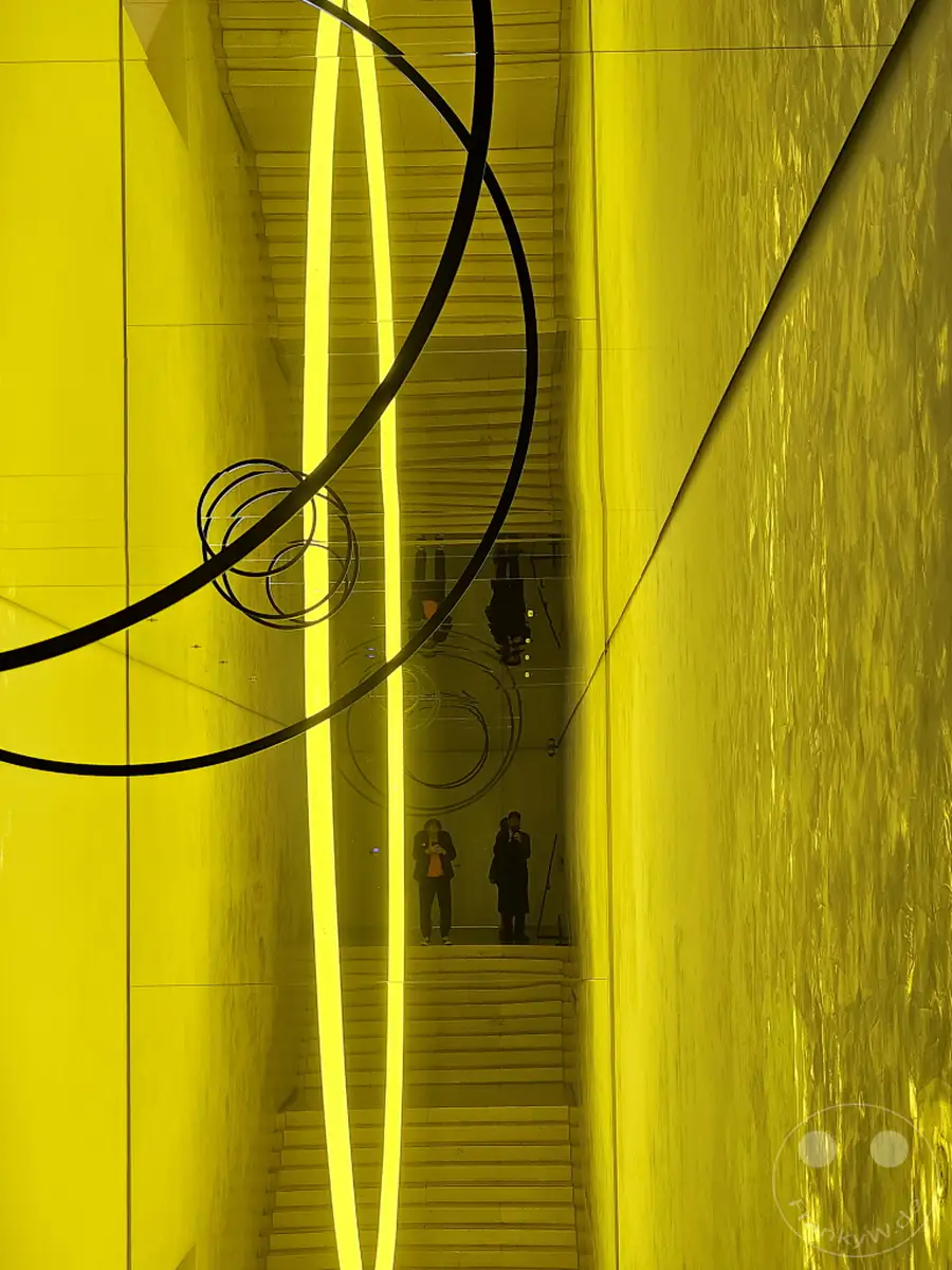 Eine beeindruckende Architekturfotografie aus Südkorea, genauer gesagt aus Seoul, fängt die minimalistische Ästhetik des Leeum Museum of Art ein. Die Szene wird dominiert von intensiven gelben Neonröhren und einer spiegelnden Oberfläche, die ein Gefühl von Weite und futuristischem Design erzeugt. Zwei Personen auf einer Treppe bieten einen menschlichen Maßstab in dieser modernen Kunstinstallation.