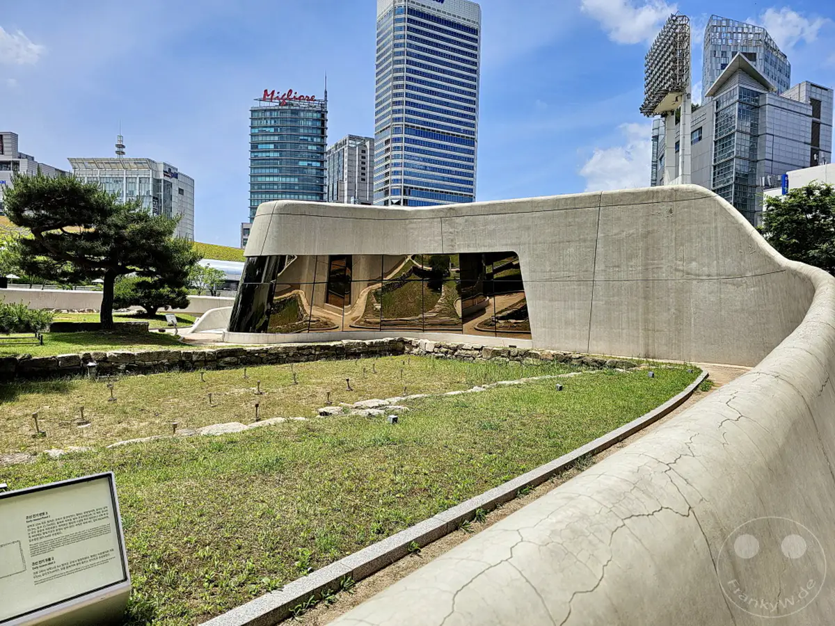 Ein Blick auf den Dongdaemun Design Plaza (DDP) in Seoul, Südkorea, wo moderne, geschwungene Architektur auf archäologische Überreste trifft. Sonnenschein beleuchtet die Szenerie und die umliegenden Hochhäuser spiegeln sich in den Glasfassaden. Die Kombination aus alt und neu schafft eine faszinierende urbane Atmosphäre.