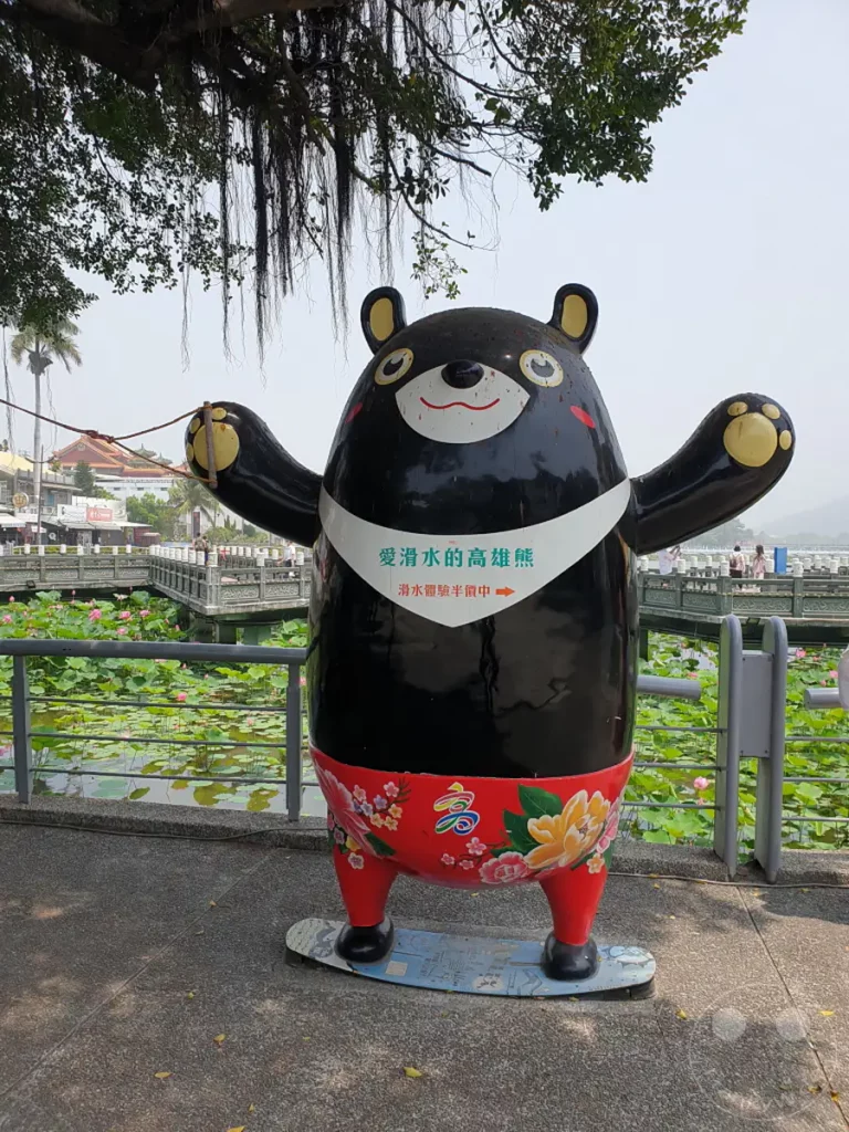 Ein auffälliges Bären-Denkmal steht vor einem Teich voller blühender Lotusblumen in Zuoying, Taiwan. Der farbenfrohe Bär mit chinesischen Schriftzeichen auf seinem Bauch und auf dem Gürtel ist ein beliebtes Fotomotiv. Die friedliche Atmosphäre des Ortes lädt zum Verweilen und Genießen der Natur ein.
