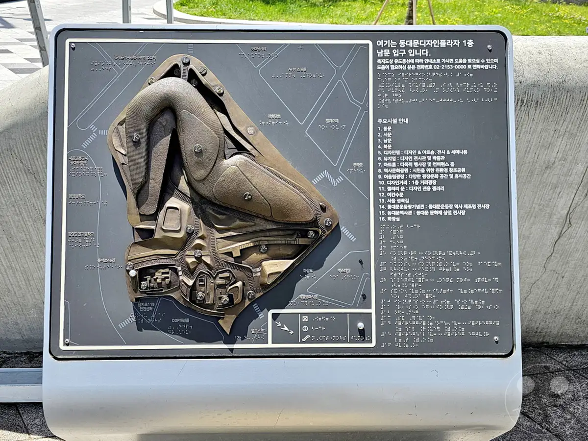 Eine taktische Orientierungstafel mit einer dreidimensionalen Karte des Dongdaemun Design Plaza (DDP) in Seoul, Südkorea. Die Tafel ist in Brailleschrift und für sehbehinderte Personen mit taktilen Elementen gestaltet. Sie bietet einen detaillierten Überblick über die verschiedenen Bereiche und Einrichtungen des DDP.