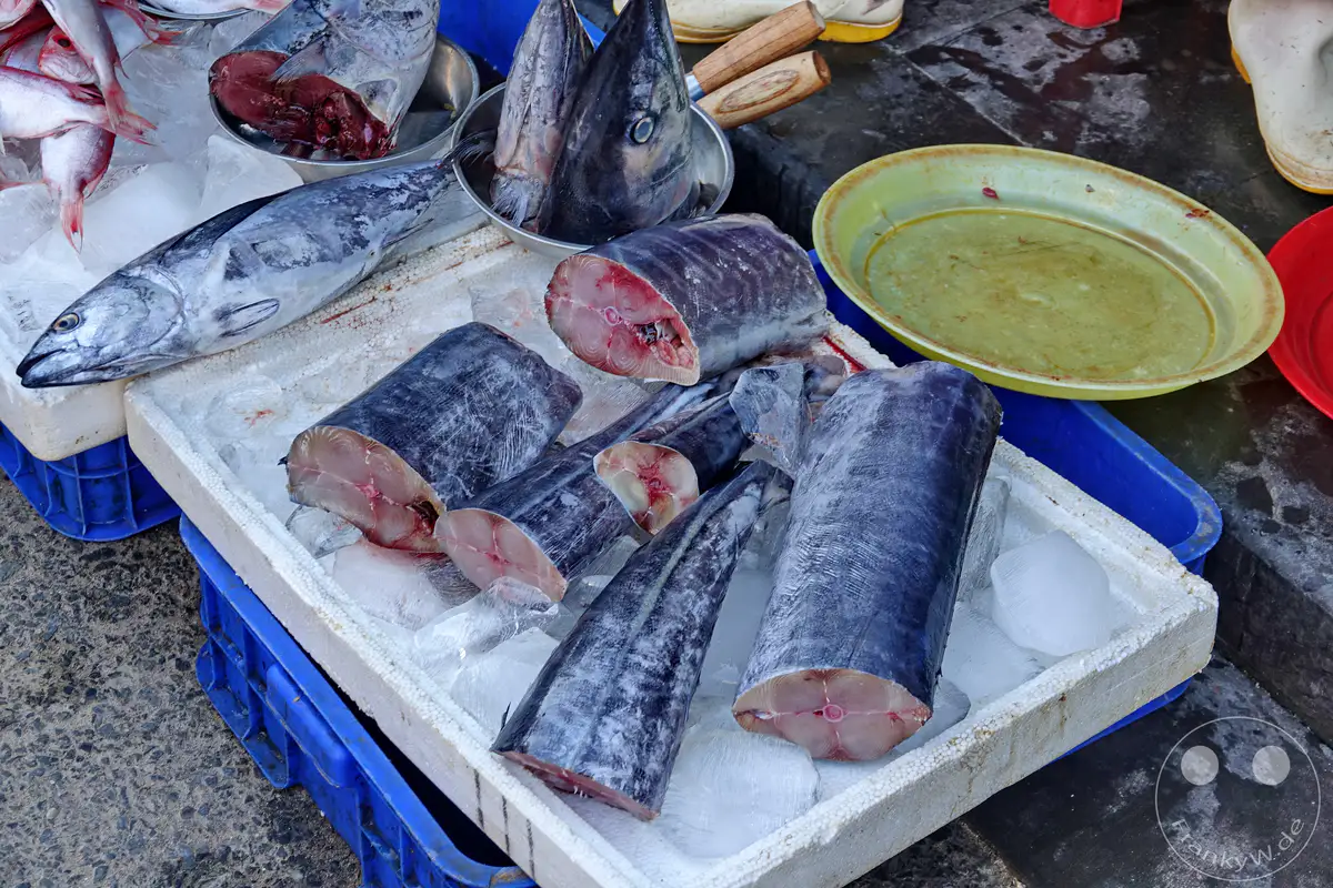 Frischer Fisch wird auf Eis in einer Auslage auf einem Markt in Hoi An, Vietnam, präsentiert. Verschiedene Fischarten, sowohl ganze Fische als auch geschnittene Stücke, liegen nebeneinander und erzeugen ein Bild der Fülle und des alltäglichen Markttreibens. Die Szenerie vermittelt die lebendige Atmosphäre eines vietnamesischen Fischmarktes.