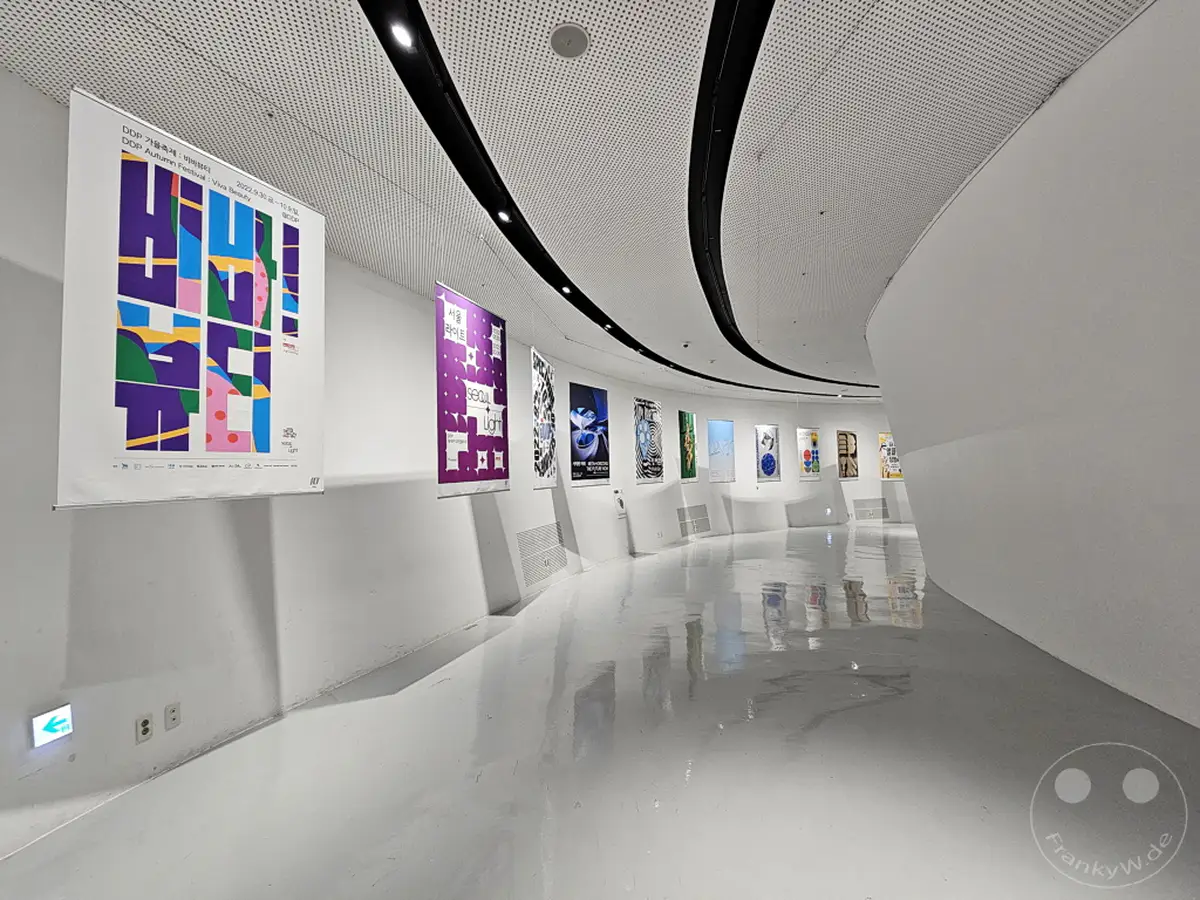 Südkorea und Seoul präsentieren sich im Dongdaemun Design Plaza (DDP) mit einer modernen Ausstellung. Der polierte Boden reflektiert die Kunstwerke und die geschwungene Architektur des Gebäudes. Eine klare und futuristische Ästhetik dominiert die Szenerie.