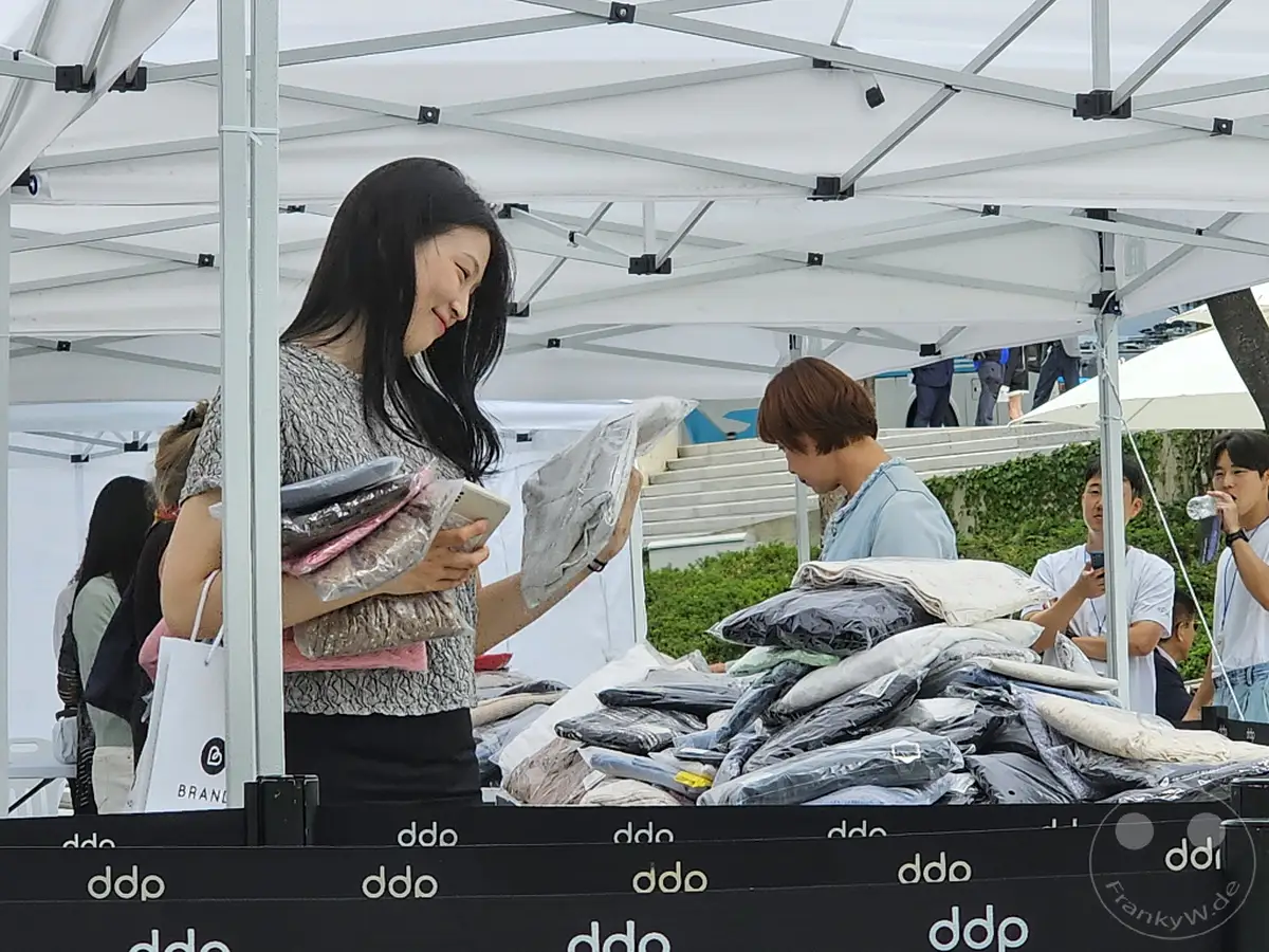 Ein Marktstand vor dem Dongdaemun Design Plaza (DDP) in Seoul, Südkorea, bietet Kleidung an. Menschen stöbern und kaufen während eines Ausverkaufs. Die Atmosphäre ist lebhaft und geschäftig, während die Kunden die Angebote begutachten.