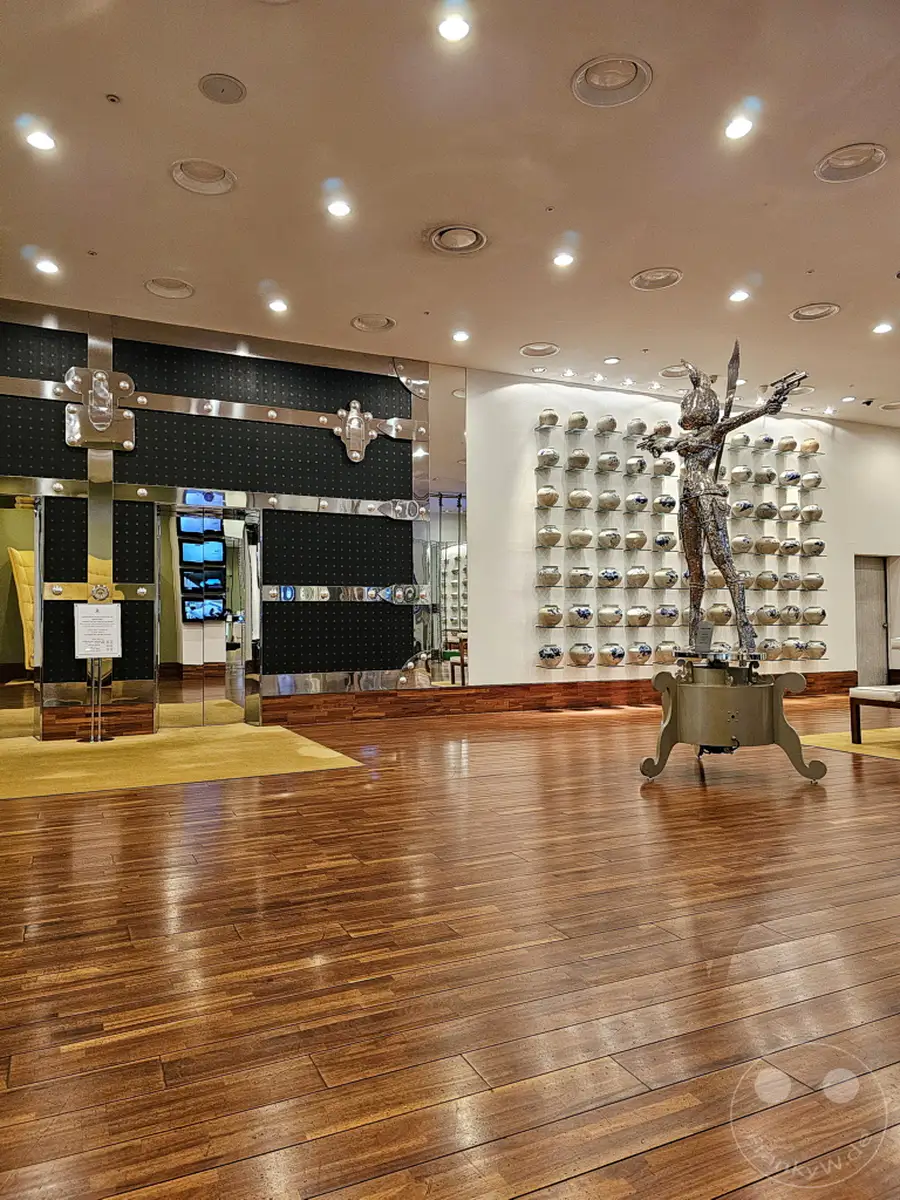 Ein glänzender Holzboden reflektiert die Beleuchtung der Decke in der Lobby des Imperial Palace Boutique Hotels in Seoul, Südkorea. Ein metallisches Kunstwerk, das einen Bogenschützen darstellt, dominiert die Mitte des Raumes, während im Hintergrund Regale mit Keramikwaren zu sehen sind. Die Szene vermittelt eine Atmosphäre von Eleganz und künstlerischem Ambiente.