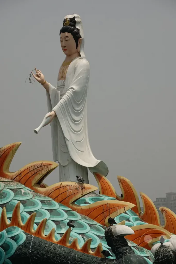 Eine imposante Statue der Guanyin steht über einer bunten Drachenskulptur in Zuoying, Taiwan, auf dem Gelände der Spring and Autumn Pavilions. Tauben sitzen auf den ornamentalen Teilen der Drachenfigur und beleben die Szenerie. Die Darstellung strahlt eine ruhige und spirituelle Atmosphäre aus, die durch die traditionelle Architektur und die friedliche Koexistenz mit der Natur unterstrichen wird.