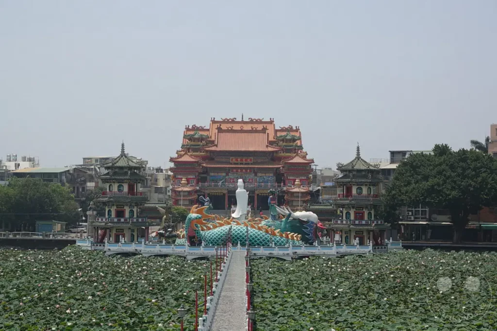 In Zuoying, Taiwan, erstreckt sich der Wuliting-See, übersät mit unzähligen Lotusblüten. Im Hintergrund erhebt sich ein beeindruckender Tempelkomplex, dessen architektonische Pracht durch die Drachen- und Götterskulpturen auf dem Wasserweg noch verstärkt wird. Die Szene strahlt eine friedliche und spirituelle Atmosphäre aus, die Besucher aus aller Welt anzieht.