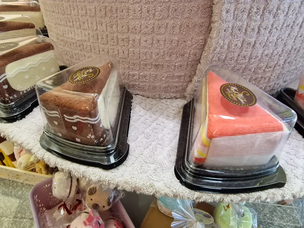 In Taiwan, Zuoying, werden Kuchenhandtücher in Auslage präsentiert, die wie köstliche Desserts aussehen. Die sorgfältige Verpackung und die detailreiche Gestaltung erwecken den Eindruck von echten Süßspeisen. Eine verspielte und kreative Präsentation für Geschenkartikel.