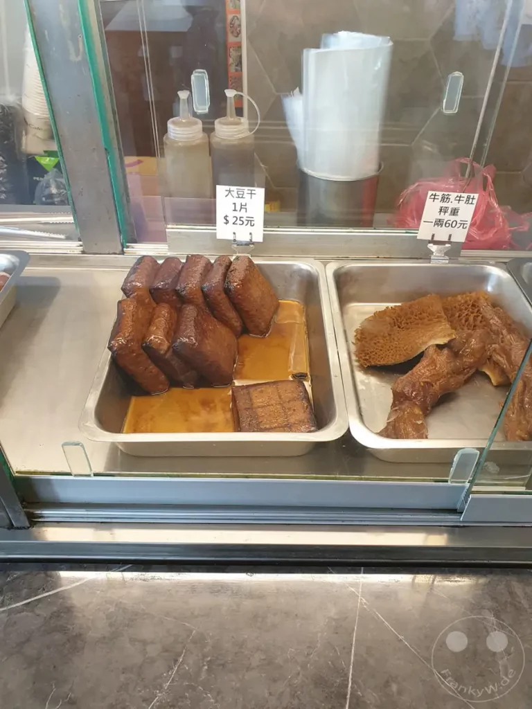 In Taiwan, in der Nähe von Zuoying, werden frisch zubereitete Tofu- und Kuttelspezialitäten zum Verkauf angeboten. Die Speisen sind in Metallbehältern aufbereitet und präsentieren sich appetitlich. Ein Blick in die Auslage verrät die Vielfalt und Frische der angebotenen Leckereien.
