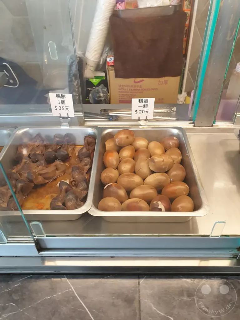 In Taiwan, genauer gesagt in Zuoying, werden herzhafte Gerichte wie Entenmägen und gekochte Enteneier zum Verkauf angeboten. Die Speisen sind appetitlich in Metallbehältern arrangiert und laden zum Probieren ein. Eine kleine Auswahl an leckeren und preiswerten Snacks ist hier für hungrige Passanten zu finden.