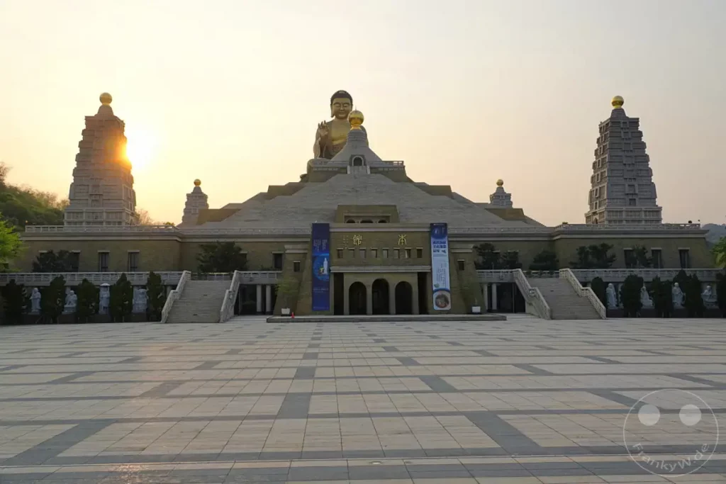 Die riesige Buddha-Statue thront majestätisch über dem Fo Guang Shan Buddha Museum in Kaohsiung, Taiwan. Die goldene Statue und die beeindruckende Architektur des Museums werden von der warmen Abendsonne beleuchtet, was eine friedliche und ehrfürchtige Atmosphäre schafft. Der weitläufige Platz davor lädt zum Verweilen und Bestaunen dieser spirituellen Stätte ein.