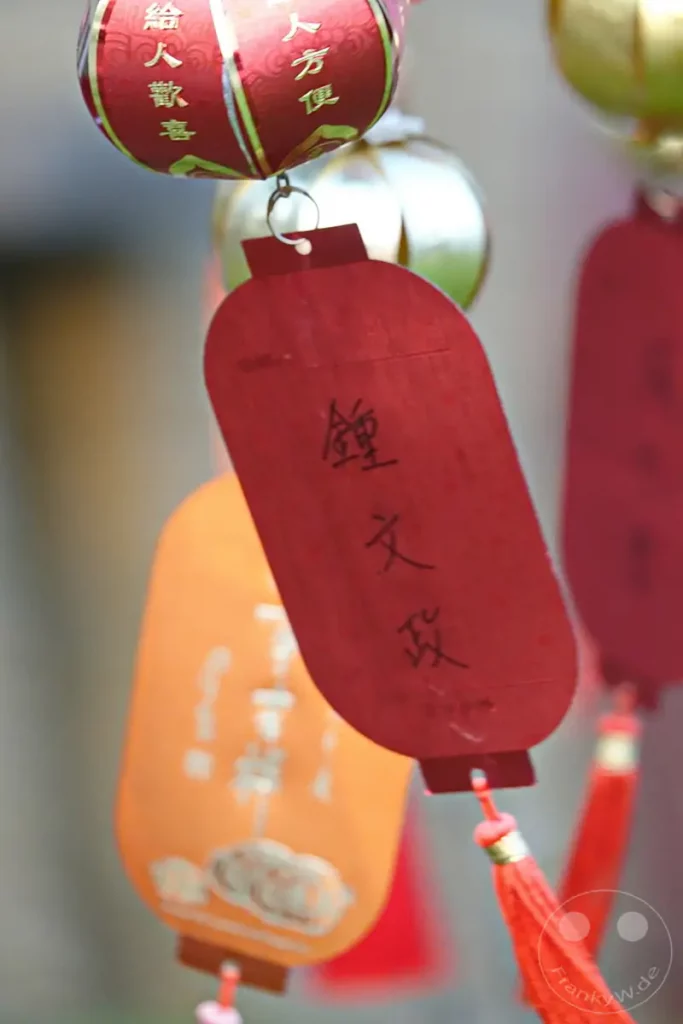 Im Fo Guang Shan Buddha Museum in Kaohsiung, Taiwan, hängen traditionelle, rot und orangefarbene Laternen und Glücksbringer. Diese Dekorationen sind oft mit Schriftzeichen verziert, die Segen oder gute Wünsche symbolisieren. Die lebendigen Farben und die detaillierten Verzierungen schaffen eine festliche und spirituelle Atmosphäre, die typisch für buddhistische Stätten ist.