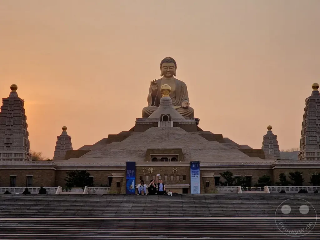 Die gewaltige Buddha-Statue thront majestätisch über der Tempelanlage des Fo Guang Shan Buddha Museums in Kaohsiung, Taiwan. In den warmen Farben des Sonnenuntergangs entfaltet sich eine friedliche Atmosphäre, während Besucher die weitläufige Treppenanlage erkunden. Die Architektur und die spirituelle Aura des Ortes laden zum Innehalten und zur Besinnung ein.