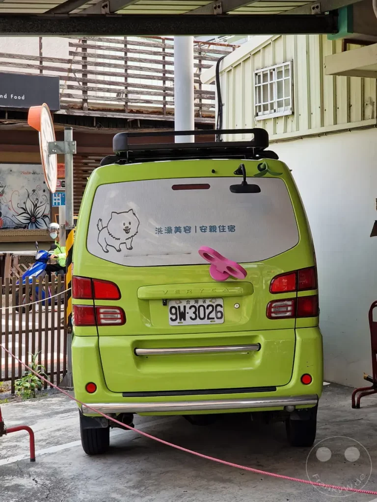 Ein leuchtend grüner Van mit dem Kennzeichen 9W-3026 steht auf einem Parkplatz in Tainan, Taiwan. Auf der Heckscheibe sind eine süße Hundezeichnung und chinesische Schriftzeichen zu sehen, daneben eine pinke Haarschleife. Die Szene strahlt eine alltägliche und freundliche Atmosphäre aus.