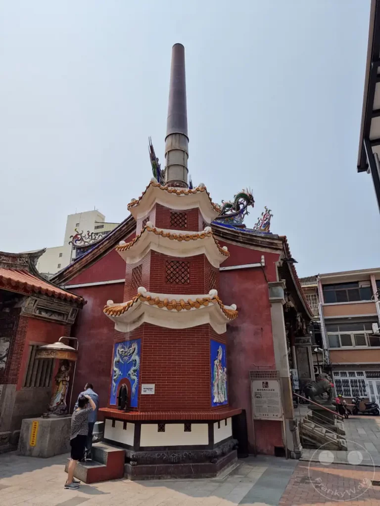 Die traditionelle Architektur des Tainan Grand Mazu Tempels in Taiwan ist von einem markanten, hohen Rauchfang geprägt, der sich über kunstvoll verzierte Dächer erhebt. Drachenskulpturen und farbenfrohe Wandmalereien zieren die Gebäude und vermitteln eine Atmosphäre von Spiritualität und kulturellem Reichtum. Mehrere Besucher betrachten die architektonischen Details und die religiösen Artefakte des geschichtsträchtigen Ortes.