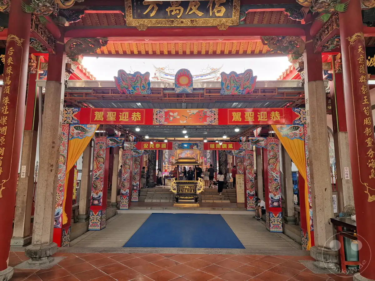 Der Tainan Grand Mazu Tempel in Taiwan zeigt eine beeindruckende traditionelle chinesische Tempelarchitektur mit leuchtend roten Säulen und aufwendigen Verzierungen. Goldene Schriftzüge und bunte Drachenmotive schmücken die Fassade und schaffen eine festliche und ehrwürdige Atmosphäre. Besucher bewegen sich durch die Gänge des Tempels, der ein wichtiges religiöses und kulturelles Zentrum darstellt.
