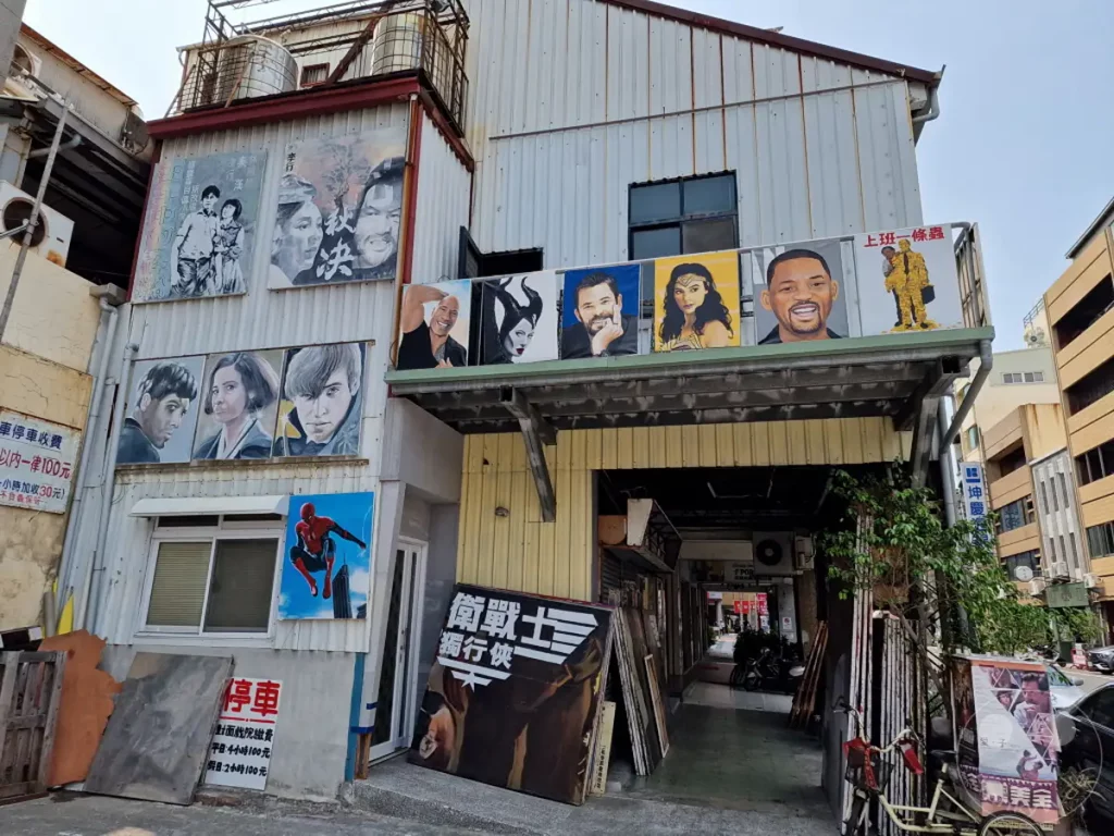Vor einer Gebäudefassade in Tainan, Taiwan, sind zahlreiche handgemalte Kinoplakate angebracht, die berühmte Schauspieler und Filmszenen darstellen. Die Werke schmücken die Außenwand und eine darüberliegende Balkonbrüstung und verleihen dem Ort einen bunten und künstlerischen Charakter. Eine Mischung aus Popkultur und lokaler Kunst strahlt eine einladende und lebendige Atmosphäre aus.