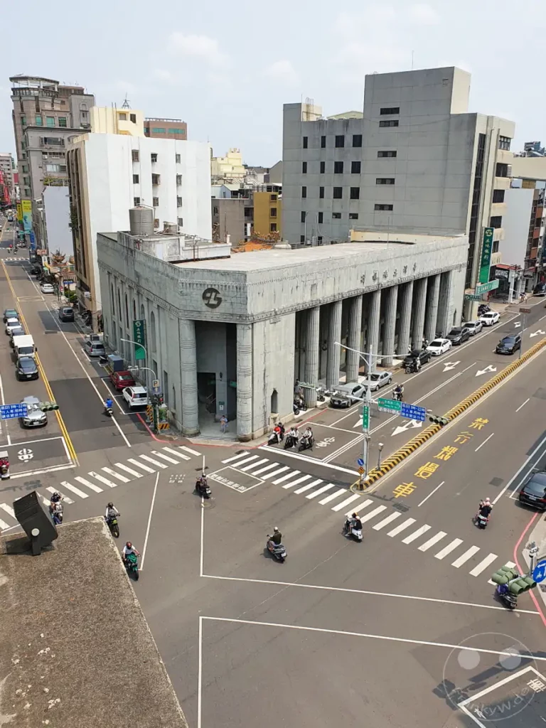 Eine belebte Straßenszene in Tainan, Taiwan, mit dem ikonischen Hayashi Department Store im Vordergrund. Motorroller bahnen sich ihren Weg durch die Kreuzung, während Fußgänger den Gehweg passieren. Die Architektur der Gebäude spiegelt eine Mischung aus traditionellem und modernem Stil wider und vermittelt ein Gefühl städtischer Vitalität.