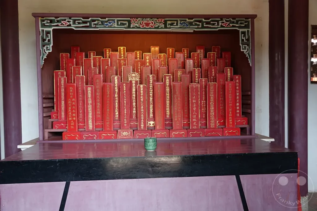 Im Inneren eines Tempels in Tainan, Taiwan, sind zahlreiche rote Gedenktafeln mit goldenen Schriftzeichen aufgereiht. Diese Tafeln, die oft Ahnen oder wichtige historische Persönlichkeiten ehren, stehen auf einem Podest vor einer reich verzierten Nische. Die Szene strahlt eine Atmosphäre der Ehrfurcht und des historischen Gedenkens aus.