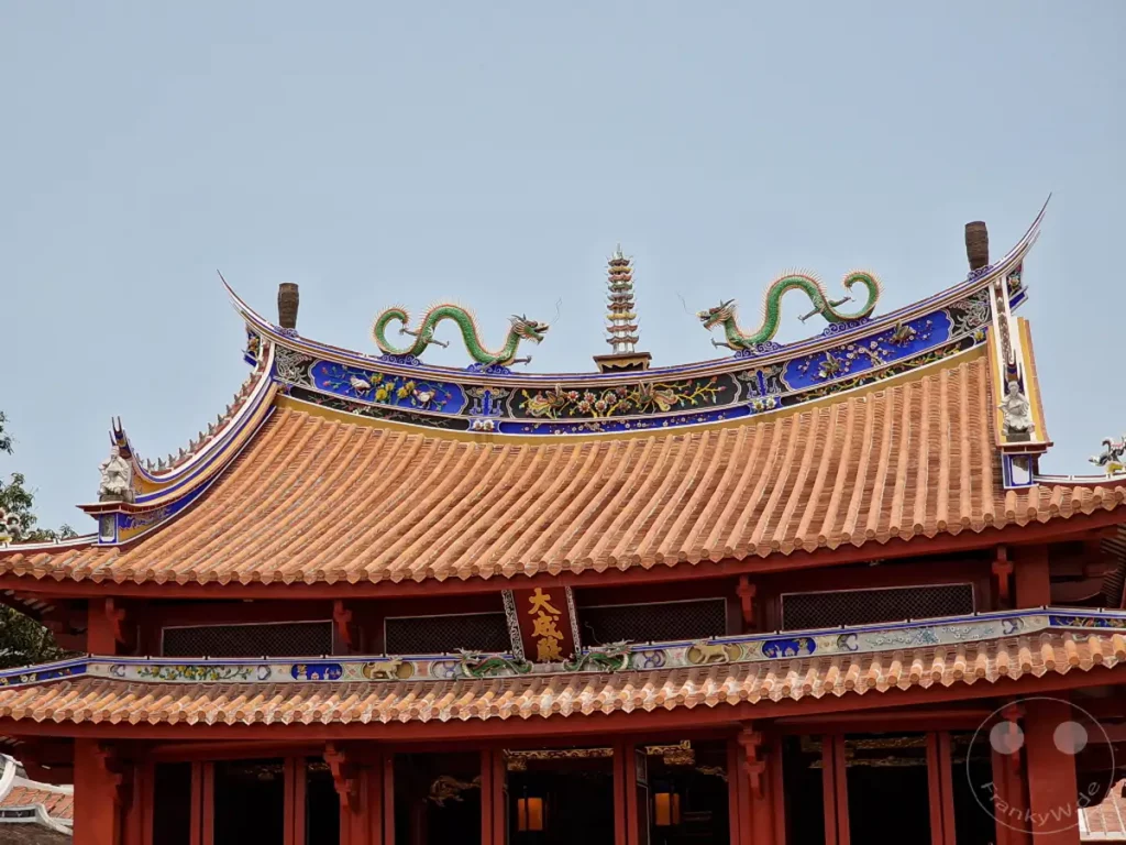 Die detailreiche Dacharchitektur des Konfuzius Tempels in Tainan, Taiwan, wird von leuchtend roten Ziegeln und kunstvoll verzierten Giebeln dominiert. Grüne Drachenfiguren schmücken die Dachkanten und symbolisieren Glück und Schutz, während feine Muster und Skulpturen die traditionelle Bauweise unterstreichen. Eine friedliche und ehrwürdige Atmosphäre geht von diesem historischen Bauwerk aus.