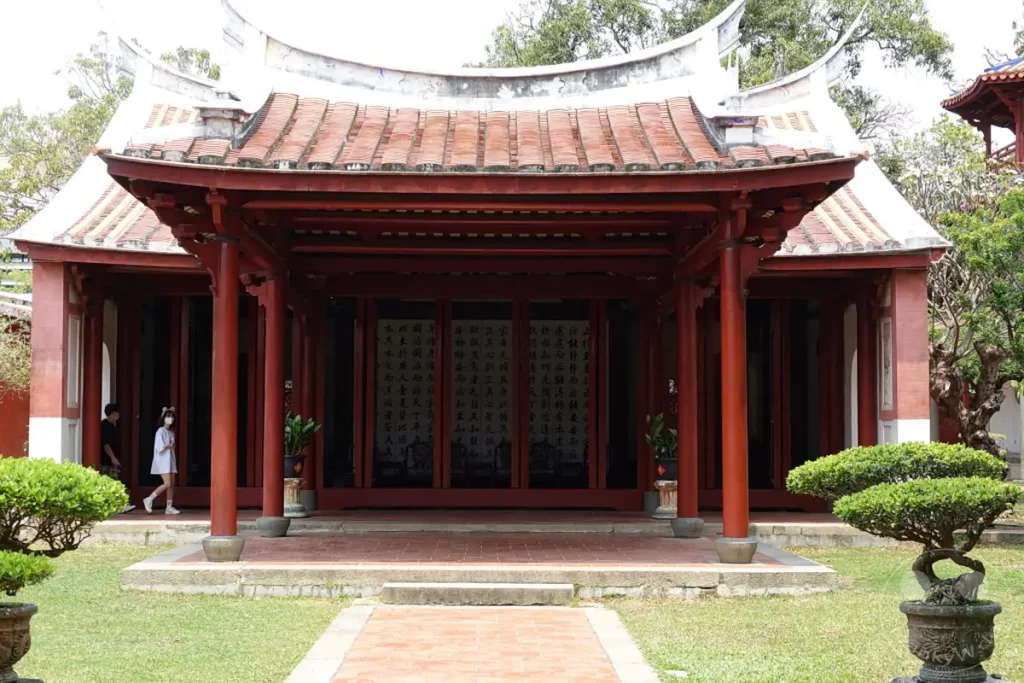 Ein traditioneller Konfuzius-Tempel in Tainan, Taiwan, mit seiner charakteristischen roten Architektur und einem gepflegten Garten. Die majestätische Struktur strahlt eine Atmosphäre der Ruhe und historischen Bedeutung aus. Besucher werden von der kunstvollen Bauweise und den kalligrafischen Schriftzeichen im Inneren angezogen.