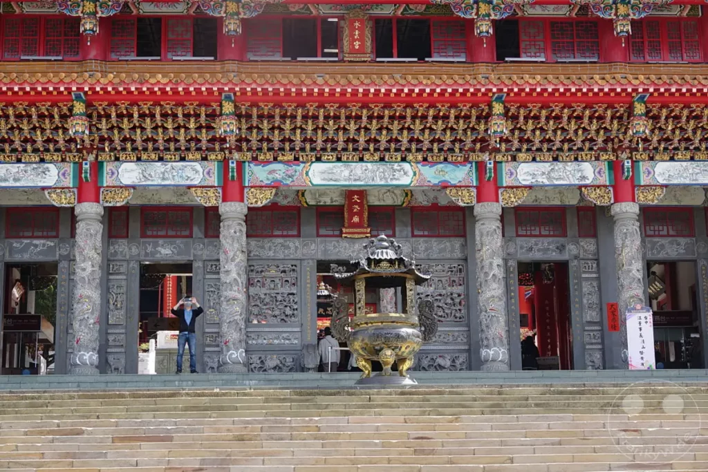 Der Wenwu Tempel am Sun Moon Lake in Taiwan beeindruckt mit seiner opulenten, roten und goldenen Architektur. Verzierungen und Skulpturen schmücken die Fassade und Säulen des imposanten Gebäudes. Die Szene strahlt eine tiefgreifende kulturelle und spirituelle Atmosphäre aus, die Besucher aus aller Welt anzieht.