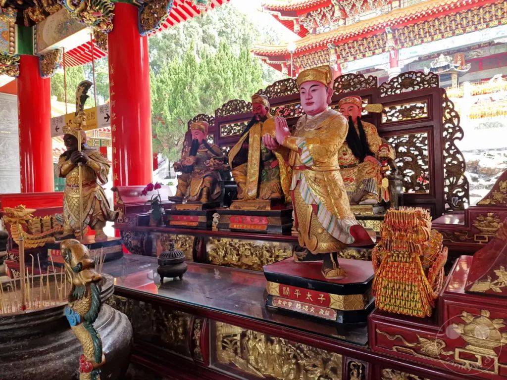 Im Wenwu Tempel am Sun Moon Lake in Taiwan sind auf einem reich verzierten Altar mehrere traditionell gekleidete Gottheiten ausgestellt. Über dem Altar spannt sich eine kunstvoll gestaltete Tempelarchitektur mit roten Säulen und geschwungenen Dächern. Die Szene strahlt eine Atmosphäre von tiefer Spiritualität und kulturellem Erbe aus.