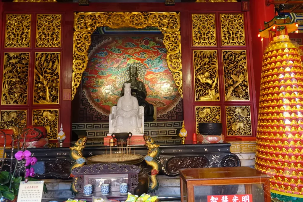 Im Inneren des Wenwu Tempels am Sun Moon Lake in Taiwan befinden sich zwei beeindruckende Statuen im Zentrum eines reich verzierten Heiligtums. Die Szenerie strahlt eine Atmosphäre der Ehrfurcht und spirituellen Ruhe aus, verstärkt durch die kunstvollen Verzierungen und die leuchtenden Farben. Vor den Statuen stehen Weihrauchschalen und Opfergaben, die auf die tief verwurzelten religiösen Traditionen der Region hinweisen.