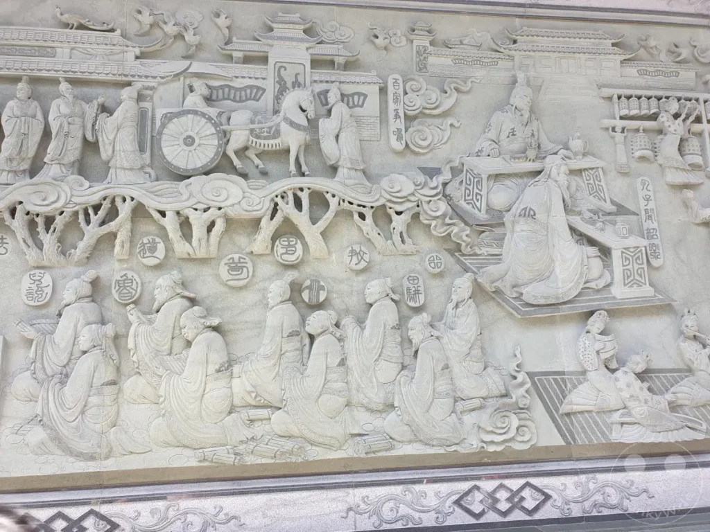 Ein detailreiches Steinrelief im Wenwu Tempel am Sun Moon Lake in Taiwan stellt eine historische Szene dar, die von Personen in traditioneller Kleidung und symbolischen Elementen geprägt ist. Die sorgfältige Ausarbeitung der Figuren und des architektonischen Hintergrunds vermittelt einen Eindruck von chinesischer Geschichte und Kultur. Die ruhige und ehrwürdige Ausstrahlung des Kunstwerks lädt zur Kontemplation über die dargestellte Epoche ein.