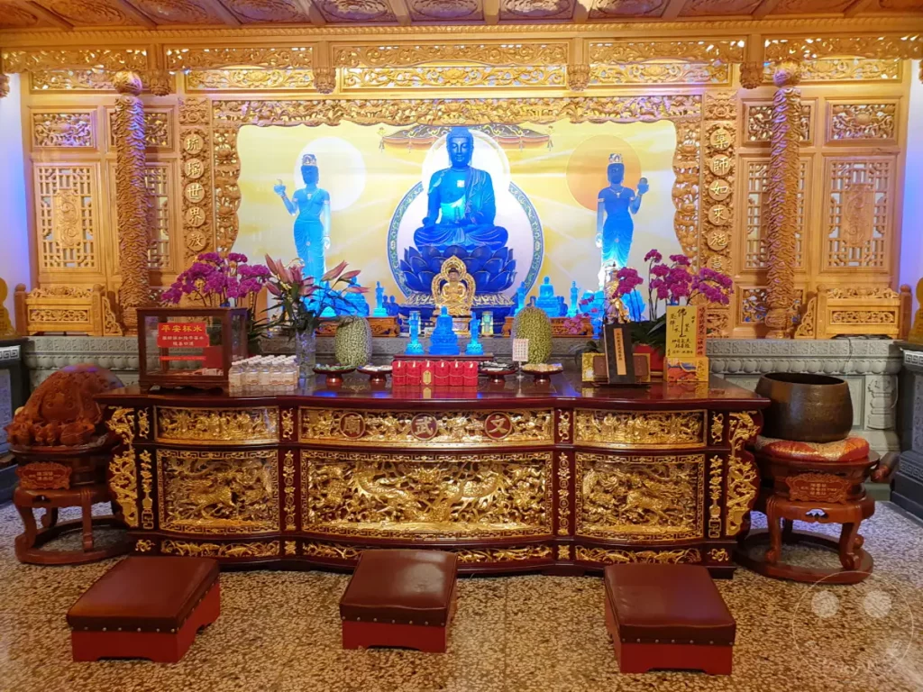 Im Wenwu Temple am Sun Moon Lake in Taiwan steht ein prunkvoller Altar im Mittelpunkt, geschmückt mit einer strahlenden Buddha-Statue und kunstvollen Holzschnitzereien. Lila Orchideen und weitere Opfergaben unterstreichen die friedliche und spirituelle Atmosphäre des Ortes. Die Szenerie strahlt eine tiefe Ruhe und Verehrung aus, typisch für buddhistische Tempel.