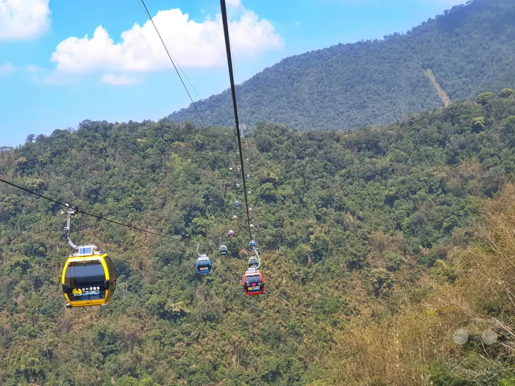 Eine Reihe von bunten Gondeln des Sun Moon Lake Ropeway schwebt über den üppig grünen Hügeln in Taiwan. Die Seilbahn verbindet die Riyuetanlan Ropeway Station mit dem Erleichterung für Reisende, die spektakuläre Ausblicke auf die umliegende Berglandschaft genießen möchten. Bei strahlendem Sonnenschein und blauem Himmel bietet diese Fahrt ein unvergessliches Urlaubserlebnis.