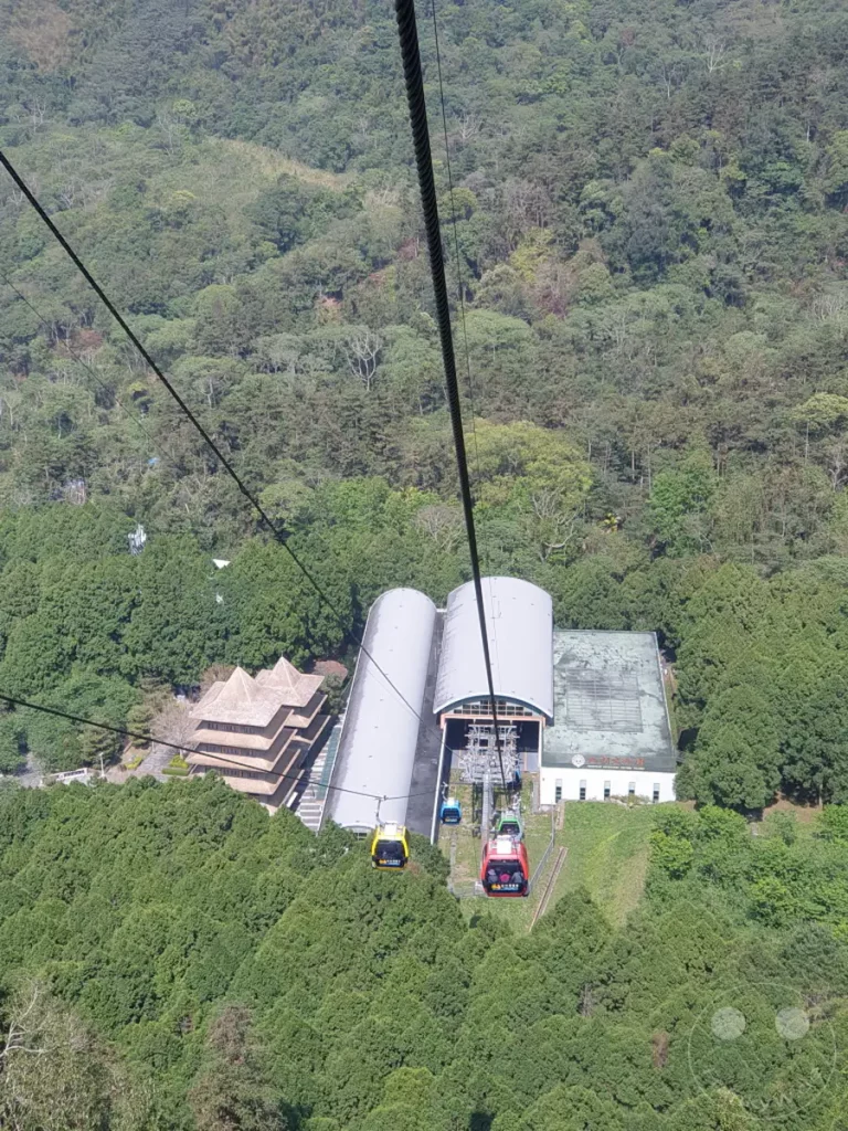 Die Riyuetanlan Seilbahnstation am Sun Moon Lake in Taiwan ist von üppiger grüner Vegetation umgeben. Mehrere Gondeln sind zu sehen, die auf ihrem Weg über die bergreiche Landschaft sind und einen Ausblick auf die Umgebung bieten. Die Szene vermittelt ein Gefühl von Ruhe und Abenteuer inmitten der Natur.