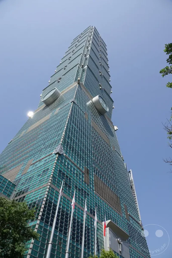 Der Taipei 101, ein ikonischer Wolkenkratzer in Taipeh, Taiwan, ragt in den strahlend blauen Himmel. Seine gläserne Fassade reflektiert das Sonnenlicht, während die markante Struktur aus verschiedenen Segmenten und den charakteristischen Uhren an den Seiten beeindruckt. Die Aufnahme vermittelt ein Gefühl von Erhabenheit und moderner Ingenieurskunst in der pulsierenden Metropole.