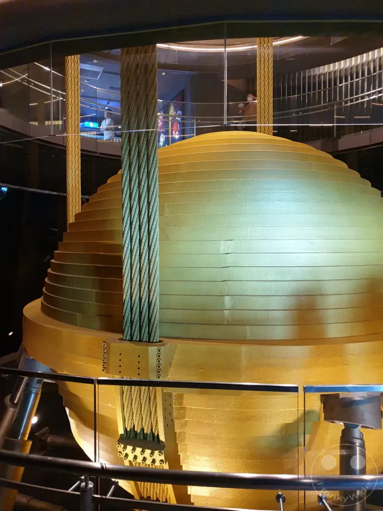 Der goldene Hauptdämpfer im Taipei 101, Taiwan, ist eine beeindruckende technische Meisterleistung, die dazu dient, Erdbeben und Taifunwinde auszugleichen. Die massive Kugel aus Stahl hängt an Stahlseilen und schwingt bei Bedarf entgegen der Bewegung des Gebäudes, um Stabilität zu gewährleisten. Dies ist ein faszinierendes Beispiel für moderne Ingenieurskunst, das Besuchern in Taipeh gezeigt wird.