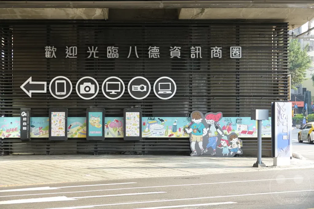 Taiwan - Taipeh, Zhongzheng District zeigt eine farbenfrohe Fassade mit digitalen Informationsdisplays und einer Wandmalerei. Mehrere stilisierte Figuren und Piktogramme deuten auf eine Verbindung zur digitalen Welt und moderner Kunst hin. Die Szene strahlt eine lebendige und einladende Atmosphäre aus und deutet auf einen kreativen urbanen Raum hin.