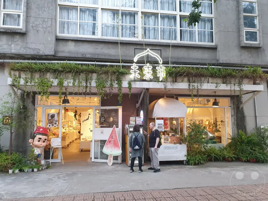 Die Fassade eines Ladens im Huashan 1914 Creative Park in Taipeh, Taiwan, präsentiert sich mit üppiger Begrünung. Hängende Pflanzen schmücken die Außenwand und den Eingangsbereich, während die Fensterfront einen Blick in das beleuchtete Innere freigibt. Eine einladende und kreative Atmosphäre geht von diesem urbanen Raum aus, der Kunst und Natur vereint.