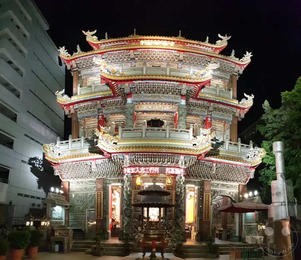 Eine kunstvoll verzierte Tempelarchitektur, beleuchtet in der Nacht in Taipeh, Taiwan. Der Jingfu Temple präsentiert sich in seiner vollen Pracht mit detailreichen Schnitzereien und leuchtenden Farben. Die Szene strahlt eine feierliche und beeindruckende Atmosphäre aus.